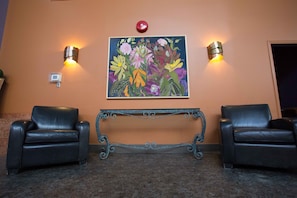 A lobby with two leather chairs, a bench, and a floral painting on the wall.