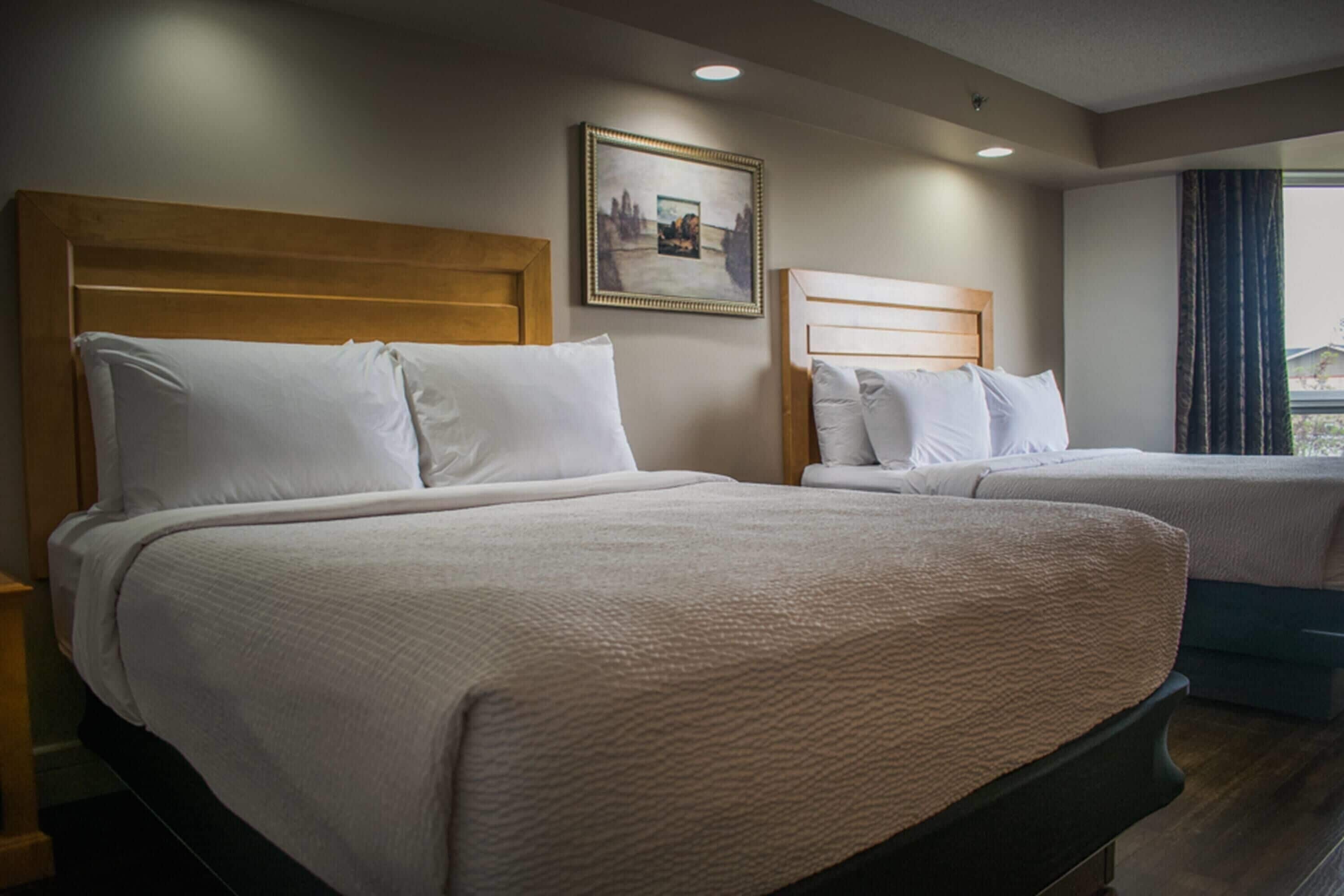 Two beds with wooden headboards, a framed picture on the wall, and a window with curtains.
