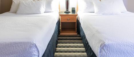 A hotel room with two beds, a nightstand with a lamp, and a striped rug.