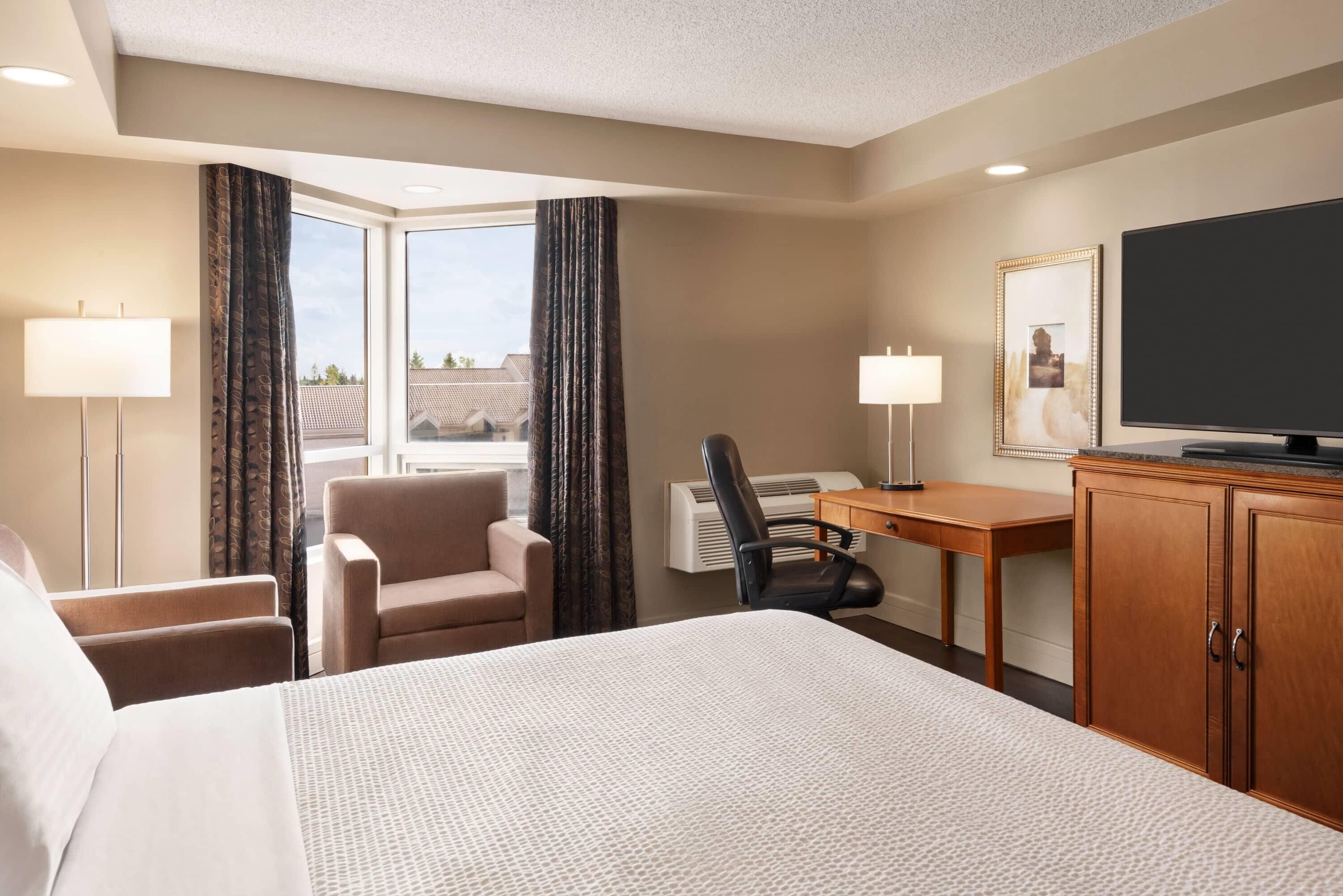 A hotel room with a bed, a desk, a chair, a television, and a window with curtains.