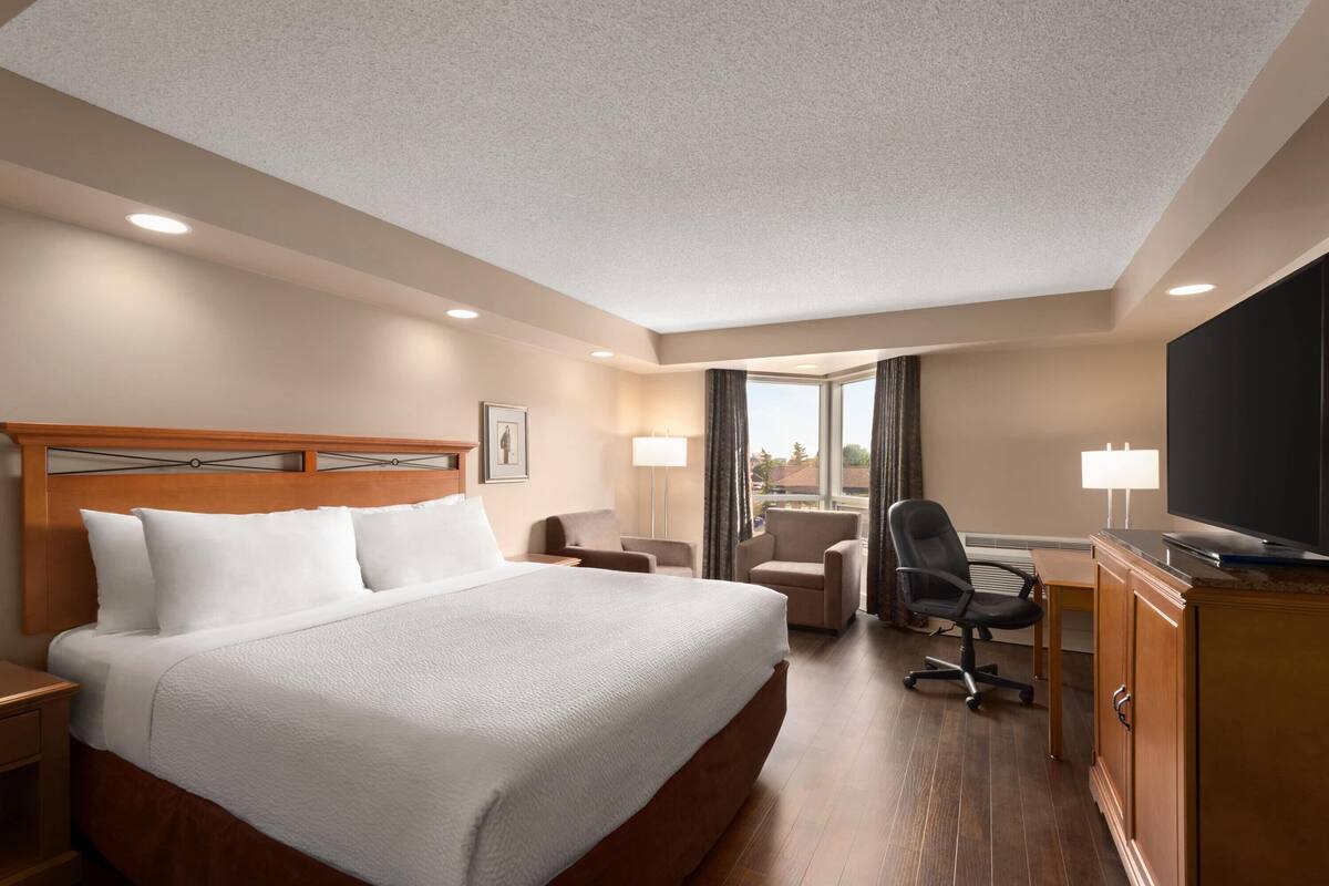 A hotel room with a large bed, a desk, a chair, a television, and a window with curtains.