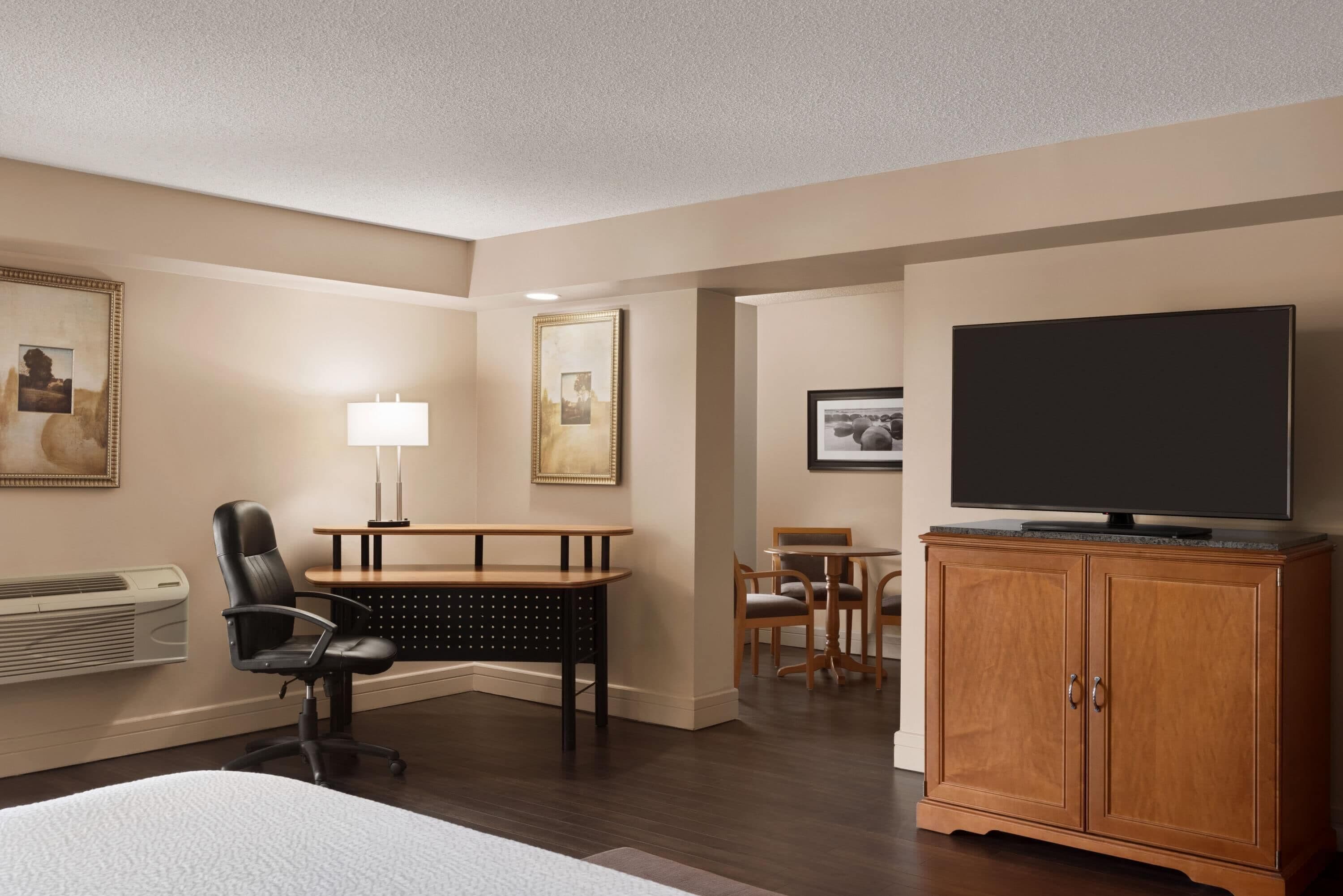 Habitación de hotel con cama, escritorio, silla, televisor y cuadros en las paredes.