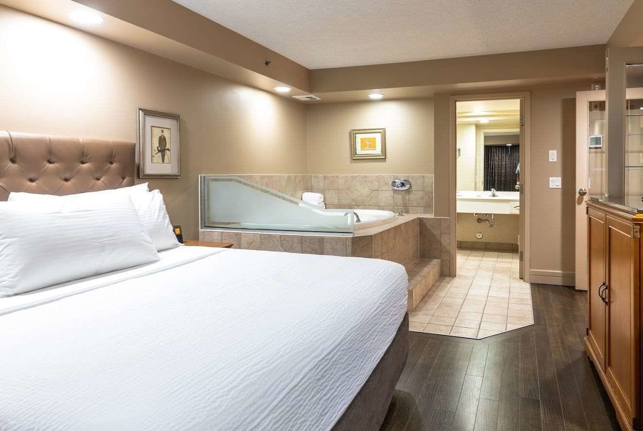 Een hotelkamer met een groot bed, een badkuip met glazen wanden, een kaptafel met spiegel en een houten kast.