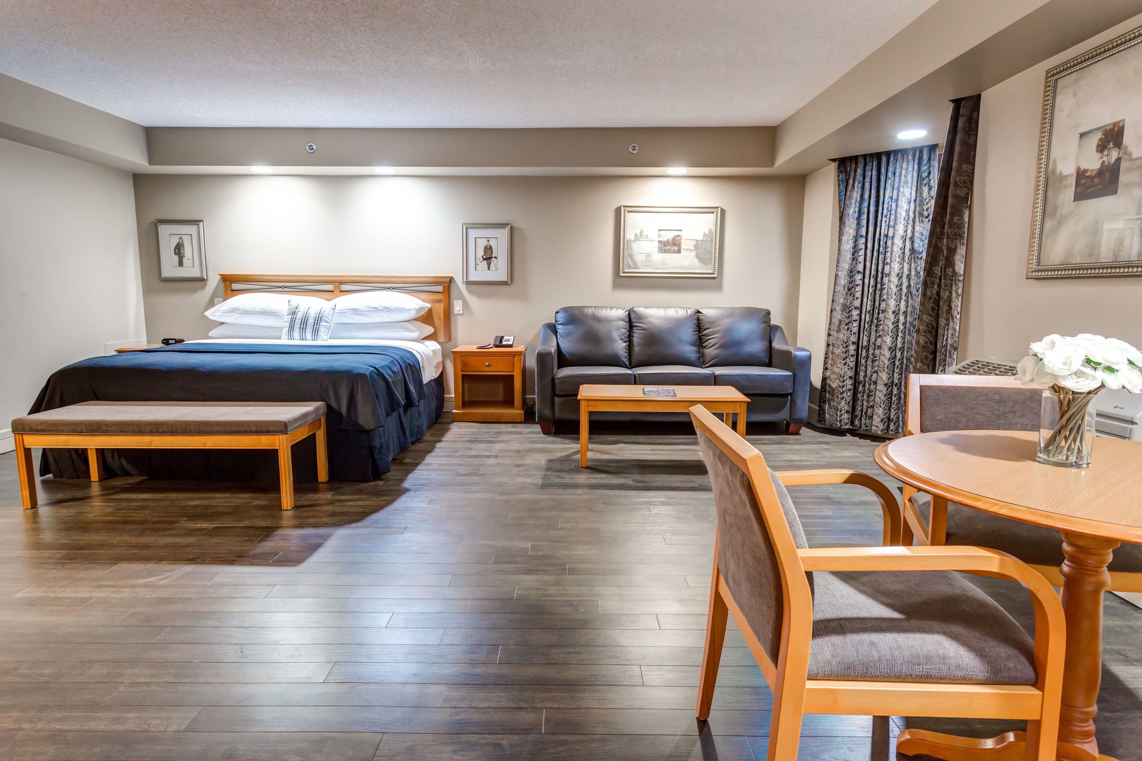 Una habitación de hotel con cama, sofá, mesa de comedor con sillas y una mesita con un florero.