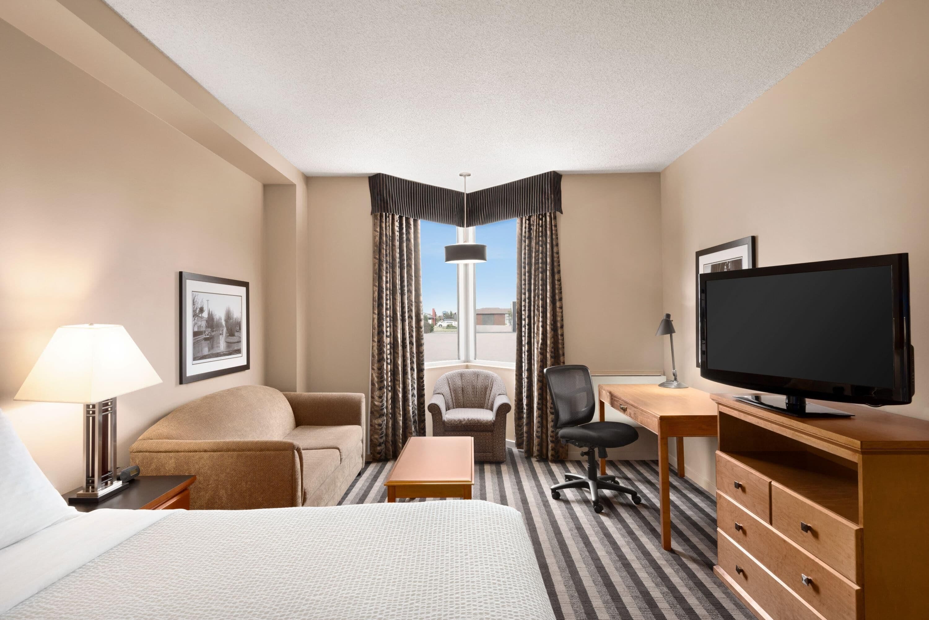 A hotel room with a bed, a desk, a chair, a television, and a window with curtains.