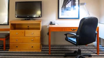 A hotel room with a wooden desk, a black office chair, a television, a telephone, and a framed picture on the wall.