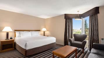 A hotel room with a bed, two bedside lamps, a chair, a table, and a large window with curtains.