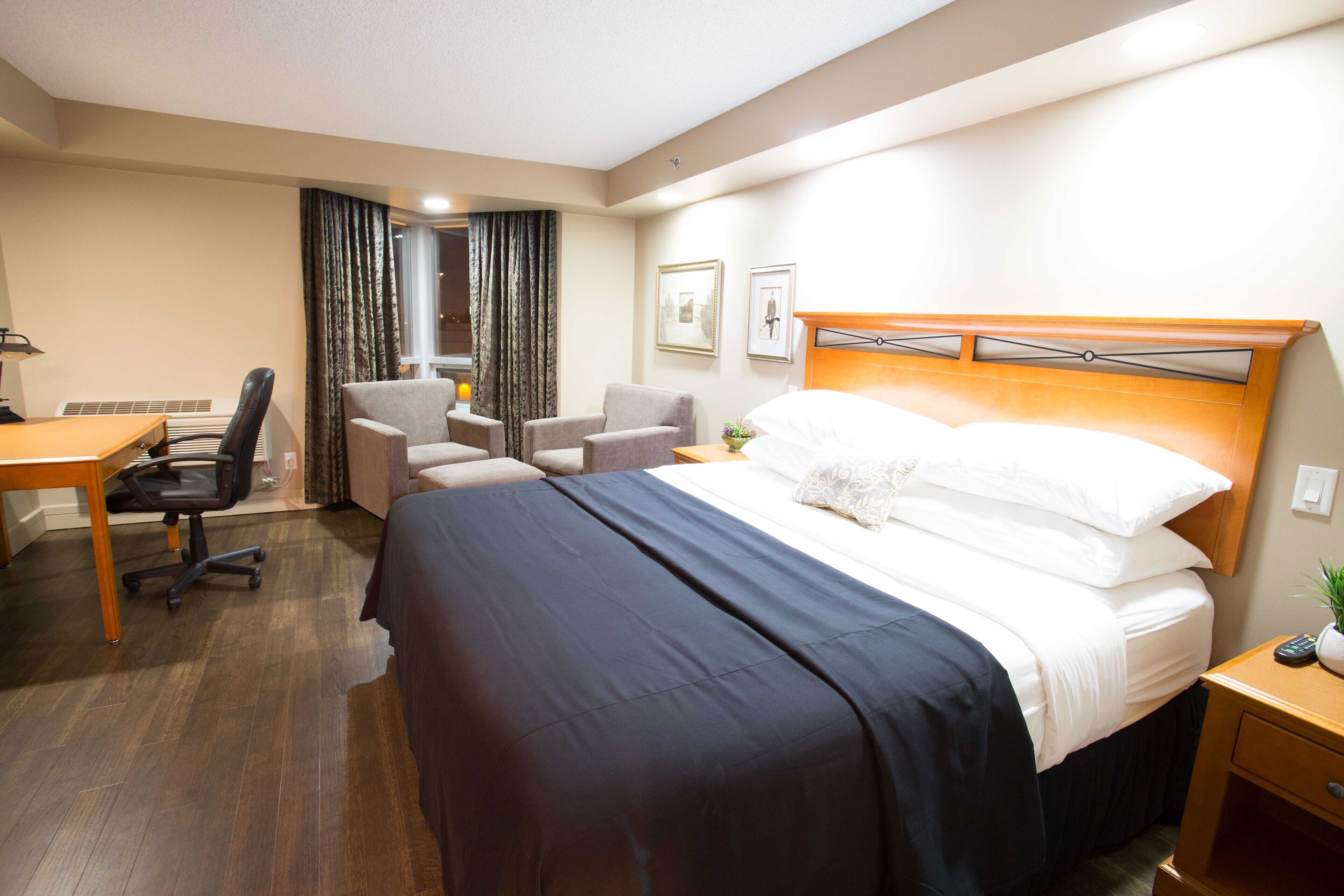 A hotel room with a bed, a desk, a chair, a small table, and a nightstand.