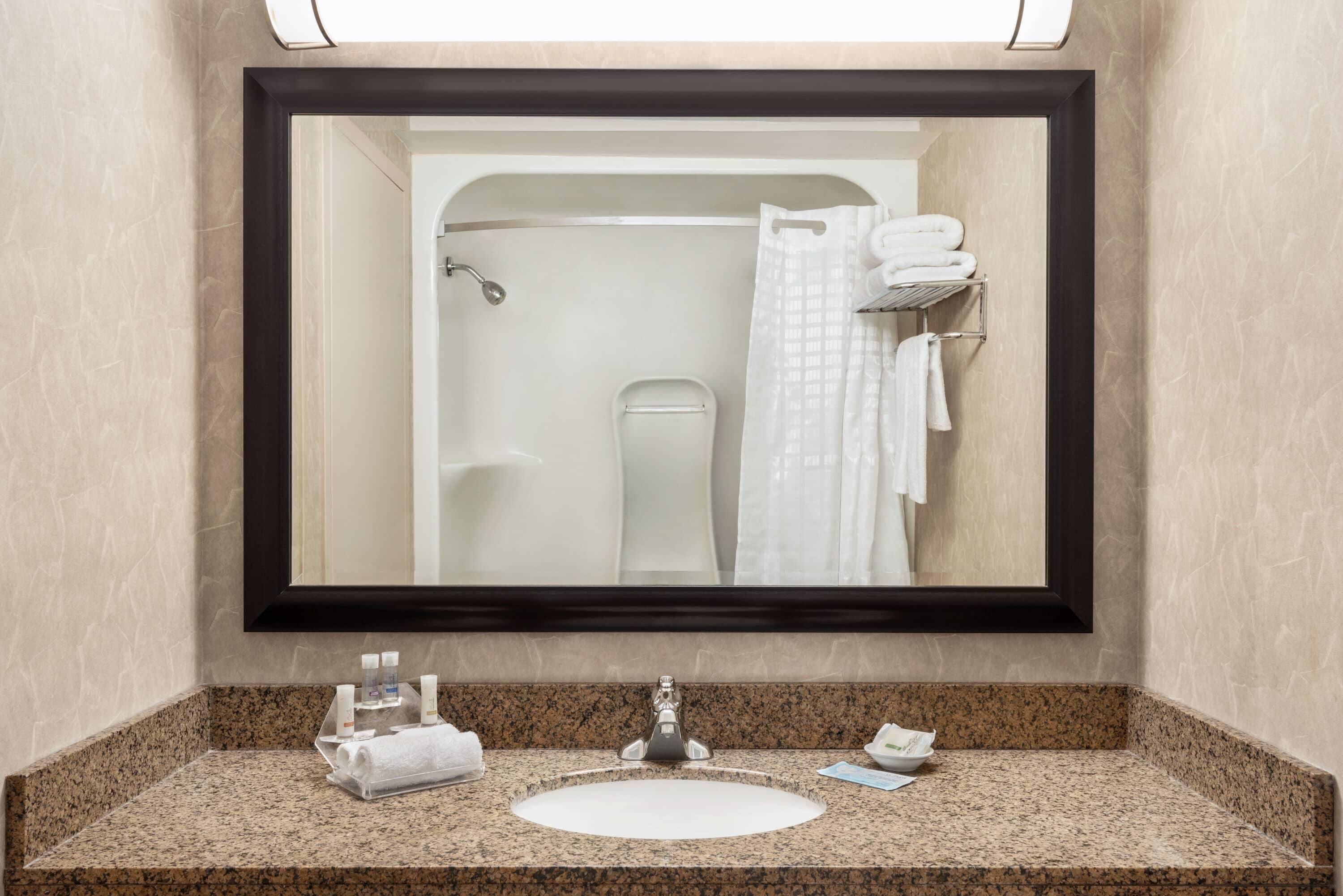 Un baño con un espejo grande, encimera de granito, lavabo, toallero y cortina de ducha.