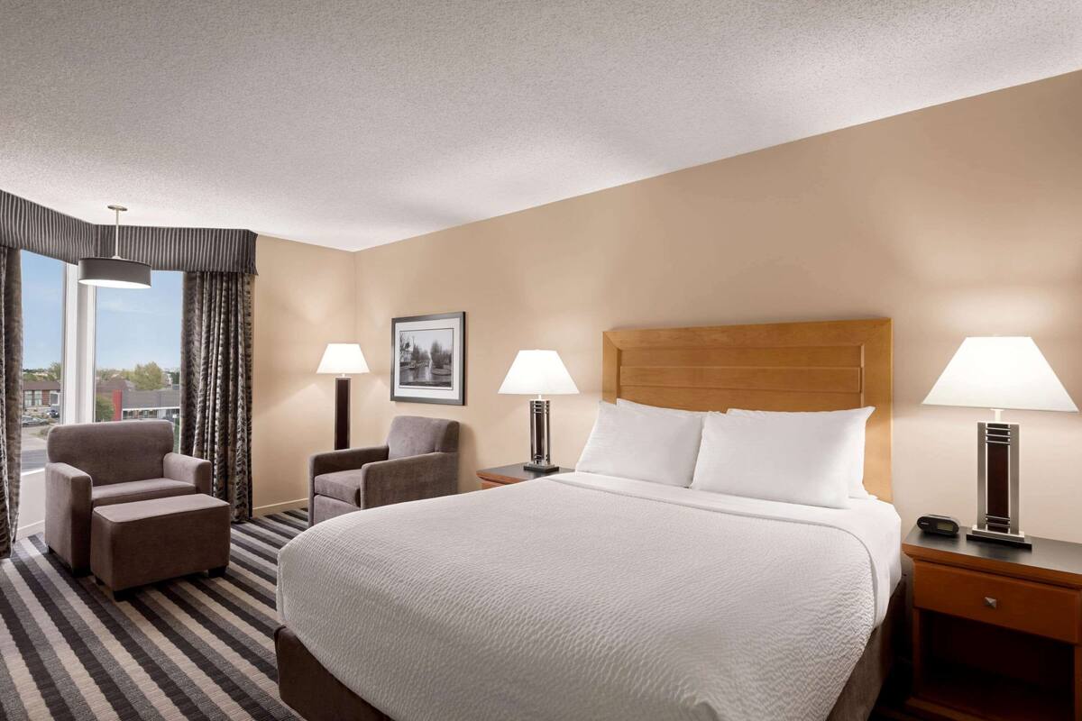 A hotel room with a large bed, two armchairs, a small table, and a nightstand with lamps.