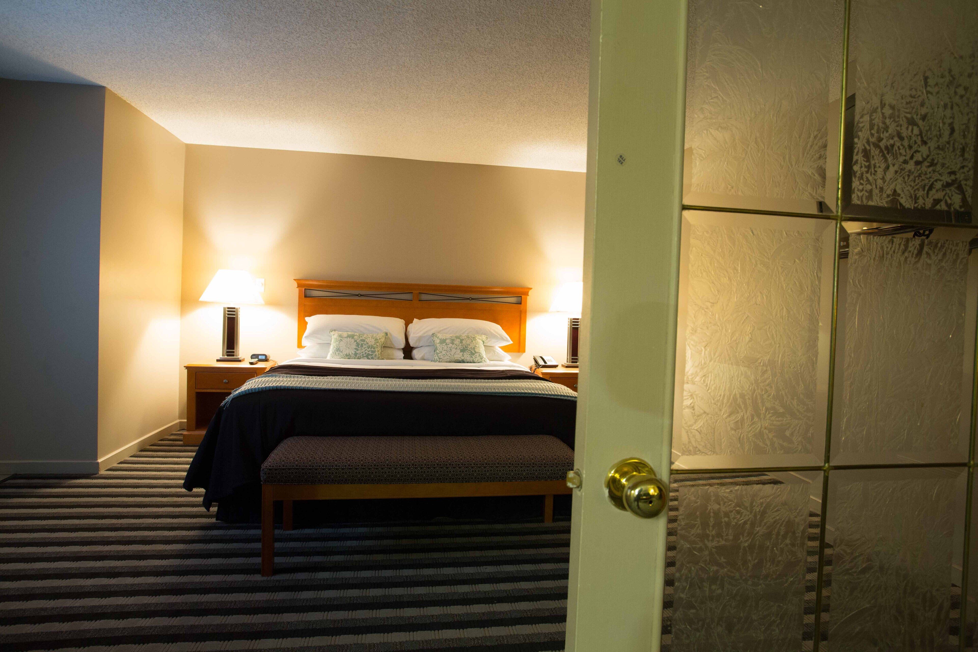 Una habitación de hotel con una cama, lámparas de noche, una mesita de noche y piso alfombrado.