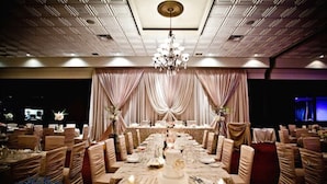 Une salle de banquet avec une longue table dressée pour un événement formel, des rideaux élégamment disposés et un lustre.