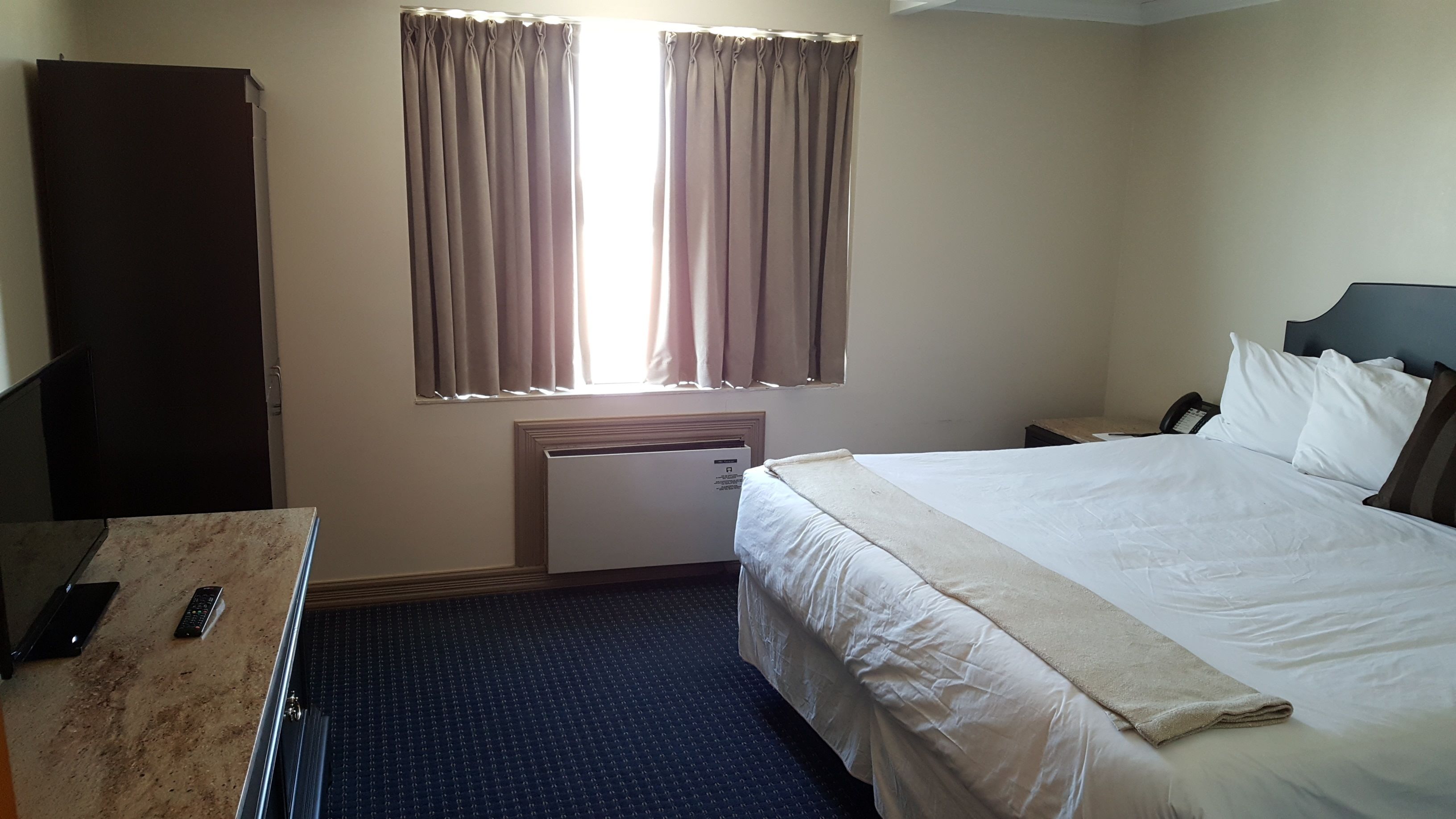 Una habitación de hotel con cama, escritorio, teléfono y ventana con cortinas.