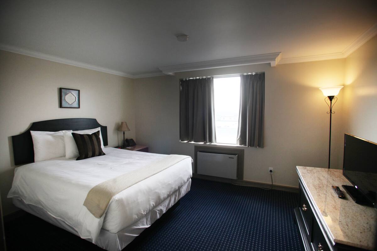 A hotel room with a large bed, a desk with a lamp, a TV, and a window with curtains.