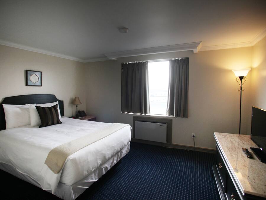 Een hotelkamer met een groot bed, een bureau met lamp, een televisie en een raam met gordijnen.