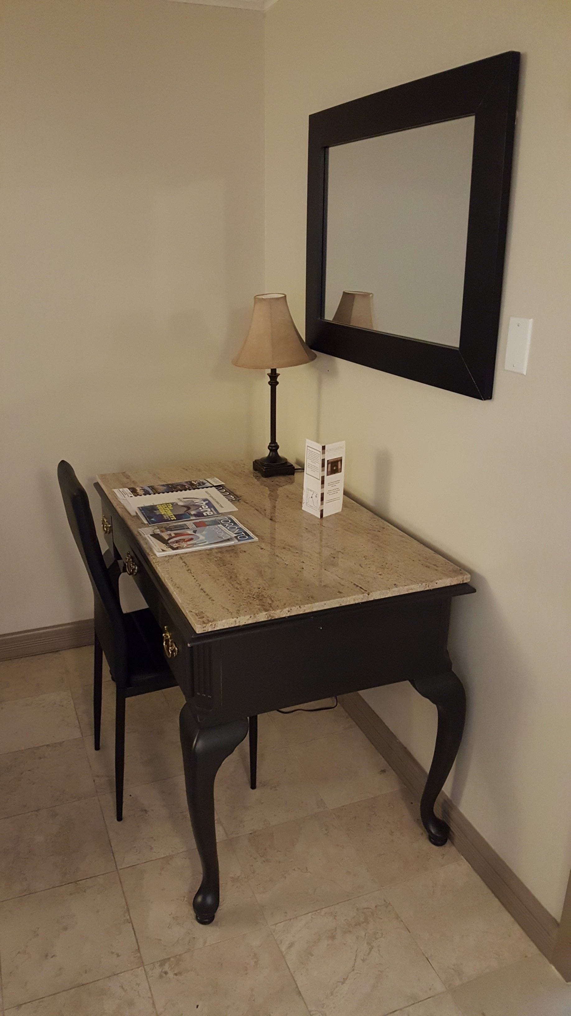 A dining table with a lamp, a chair, and a mirror on the wall.