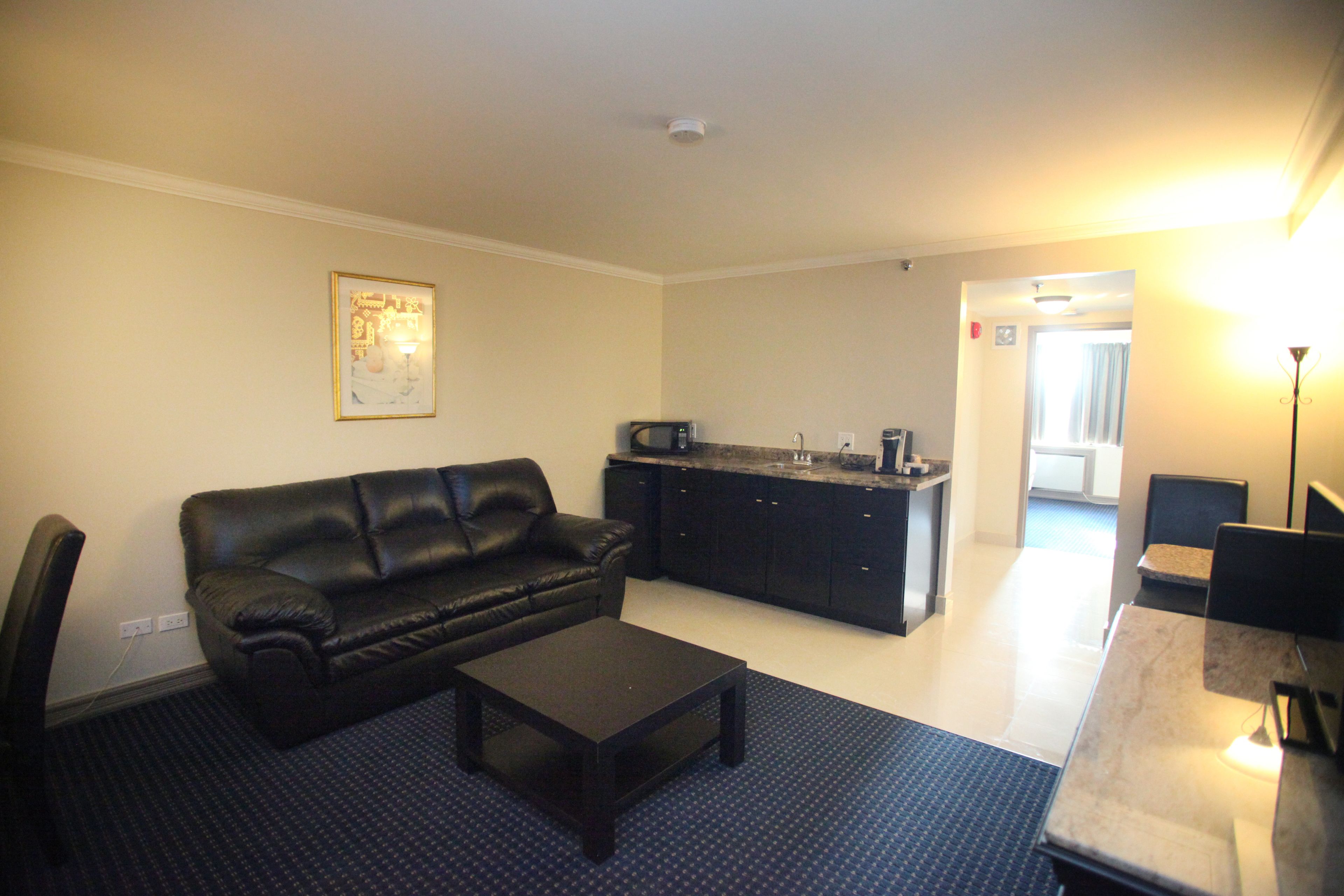 A living room with a black leather sofa, a coffee table, a dining table, and a kitchen area with a microwave.