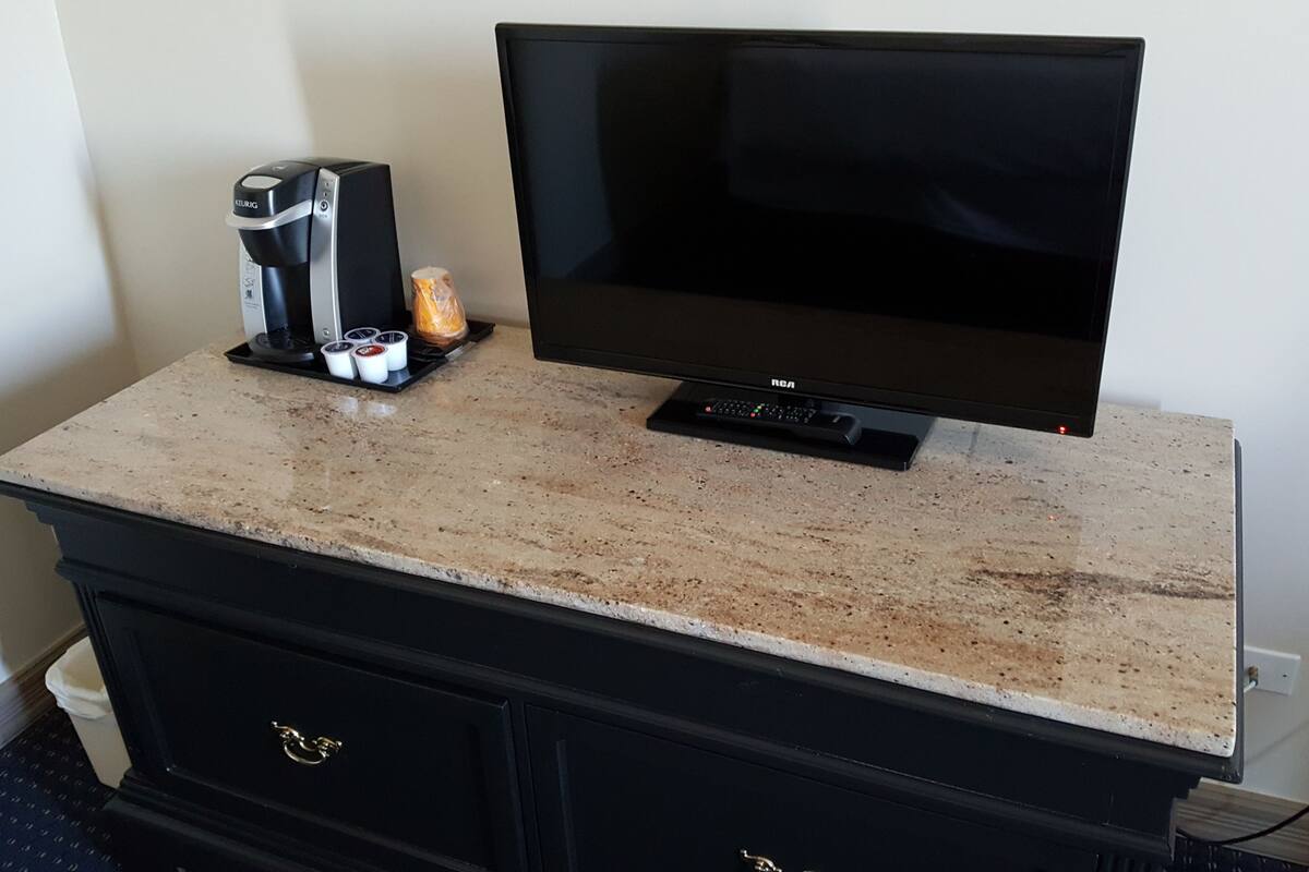 A flat-screen TV on a granite countertop, a coffee maker, and a remote control.