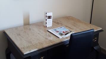 A hotel room with a desk, two chairs, a mirror, a lamp, and a small table with a magazine.