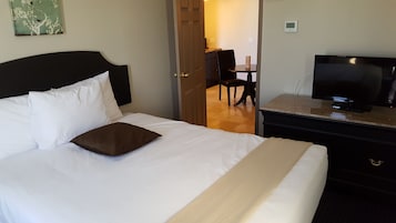 Een hotelkamer met een bed, een televisie op een dressoir en een deur naar een eethoek.