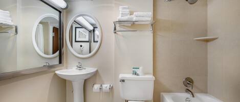 Un baño moderno con lavamanos pedestal, inodoro y bañera. Hay toalleros y un espejo.