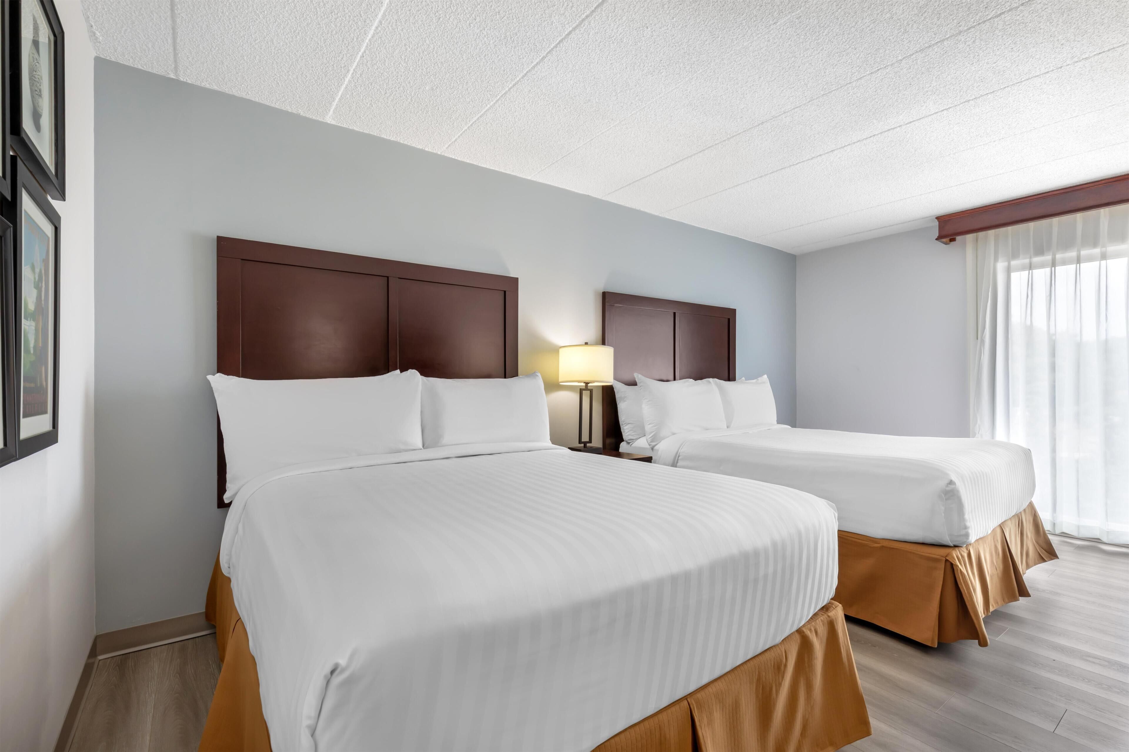 Ein Hotelzimmer mit zwei Betten, einem Nachttisch mit Lampe und einem Fenster mit Vorhängen.