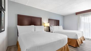 Ein Hotelzimmer mit zwei Betten, einem Nachttisch mit Lampe und einem Fenster mit Vorhängen.