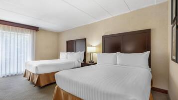 Quarto de hotel com duas camas, uma mesinha de cabeceira, uma luminária e uma janela com cortinas.