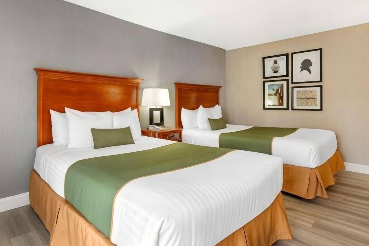 A hotel room with two beds, a nightstand with a lamp, and framed artwork on the wall.