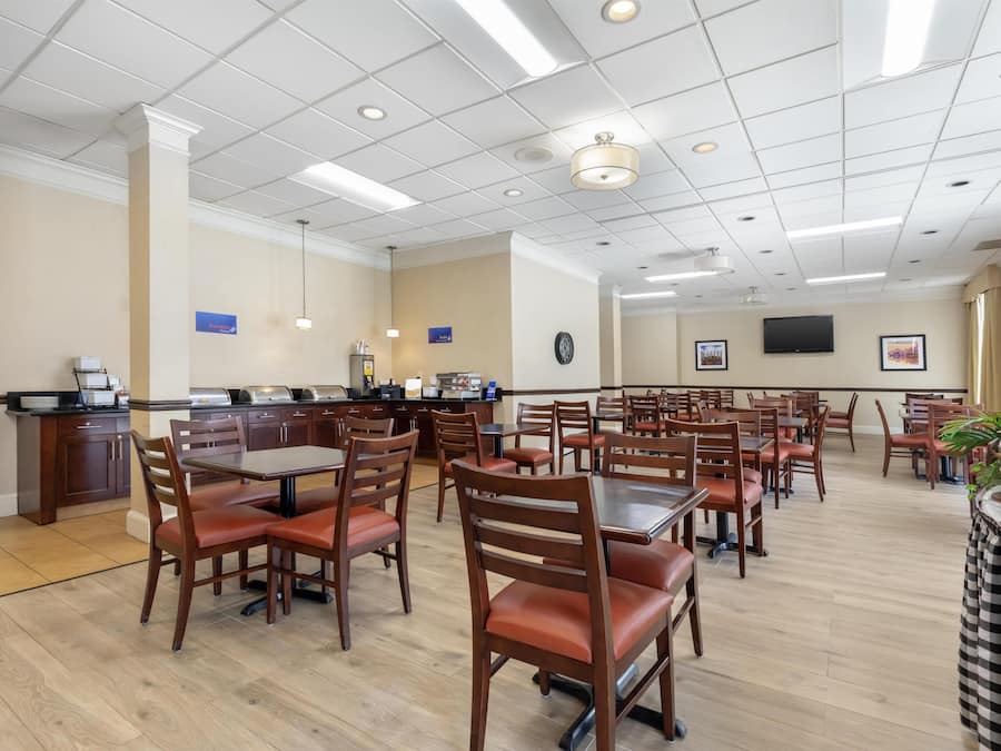 A dining area with multiple tables and chairs, a kitchen area with appliances, and a television mounted on the wall.