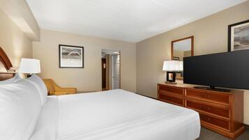 A hotel room with a bed, a television on a wooden dresser, a chair, and a door leading to another room.
