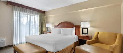 Habitación de hotel con una cama grande, dos mesitas de noche con lámparas, un banco y una silla.