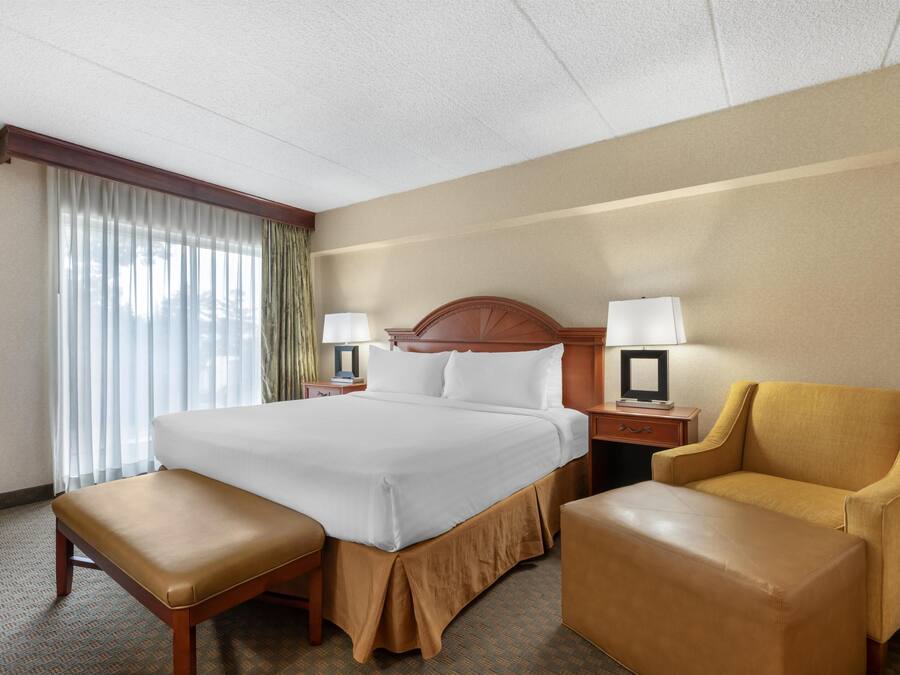 A hotel room with a large bed, two bedside tables with lamps, a bench, and a chair.