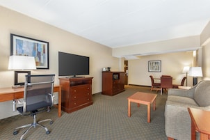 A hotel room with a desk, chair, television, dresser, and a sofa.