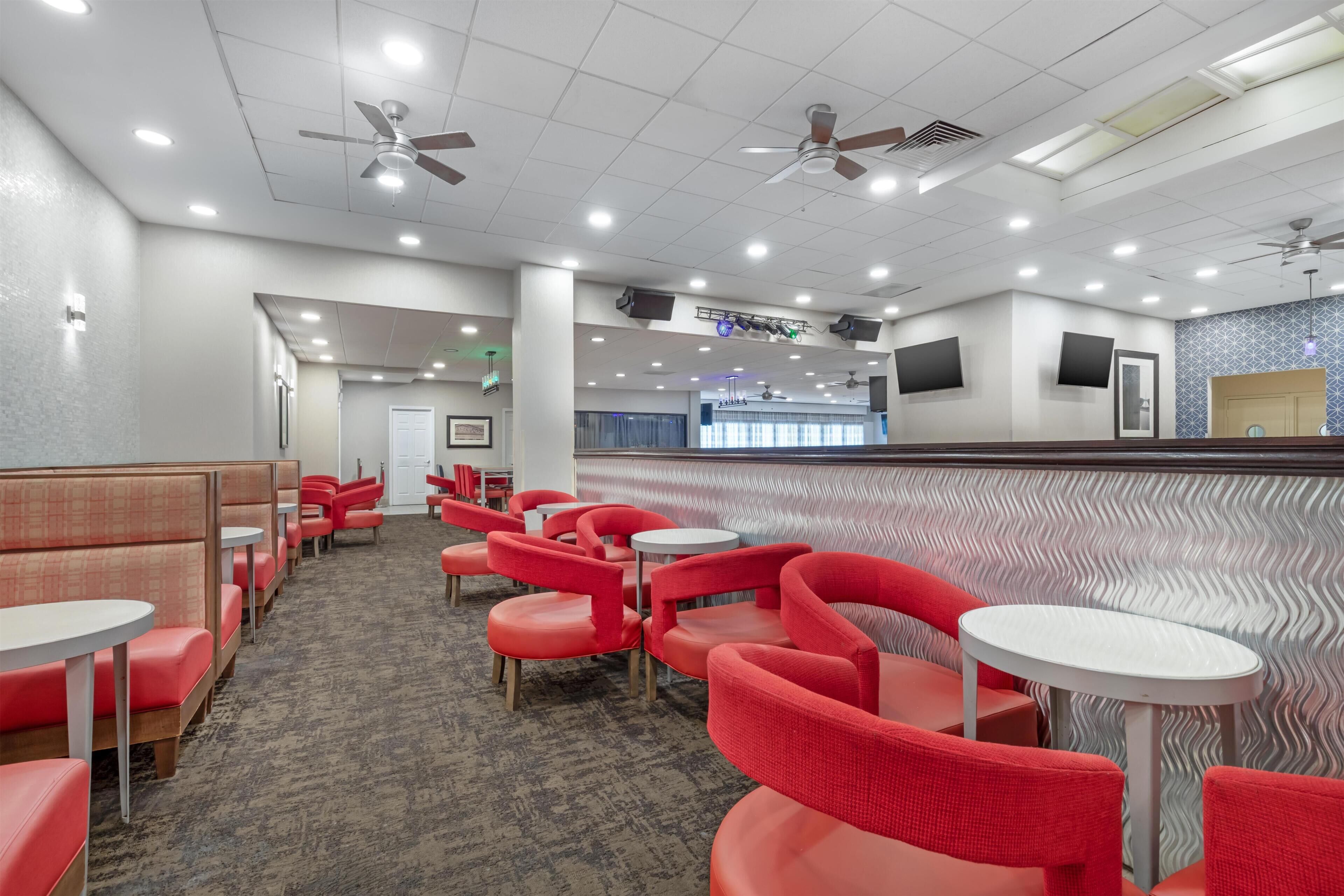 A hotel lobby with red seating, ceiling fans, recessed lighting, and a patterned wall.