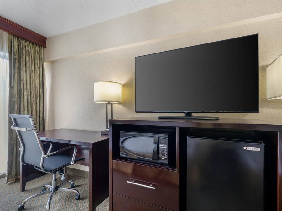 A hotel room with a desk, chair, television, and a minibar.