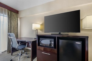 Habitación de hotel con escritorio, silla, televisor y minibar.