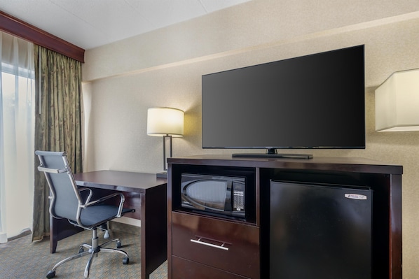 Habitación de hotel con escritorio, silla, televisor y minibar.