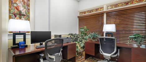 A hotel office with two desks, computers, chairs, and decorative plants.