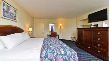 A hotel room with a large bed, a wooden dresser, a desk, a chair, and a television on the wall.