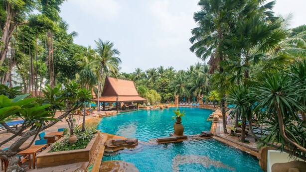 A pool area with a tiled floor, surrounded by palm trees and a building with a red roof. - Avani Pattaya Resort (Pattaya)