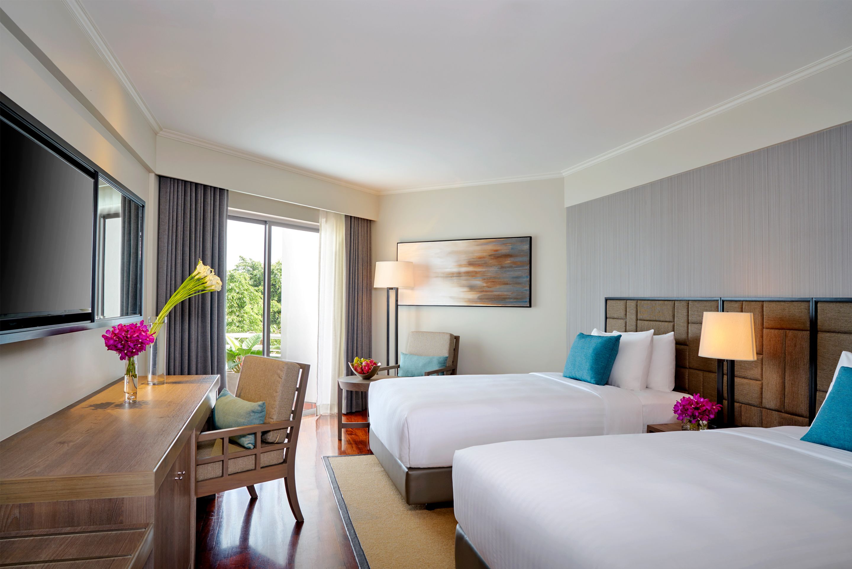 A hotel room with two beds, a desk, a chair, a TV, and a window with curtains.