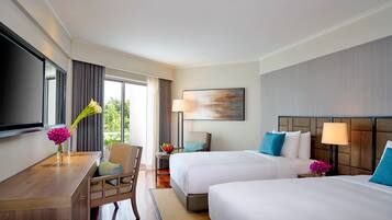 A hotel room with two beds, a desk, a chair, a TV, and a window with curtains.