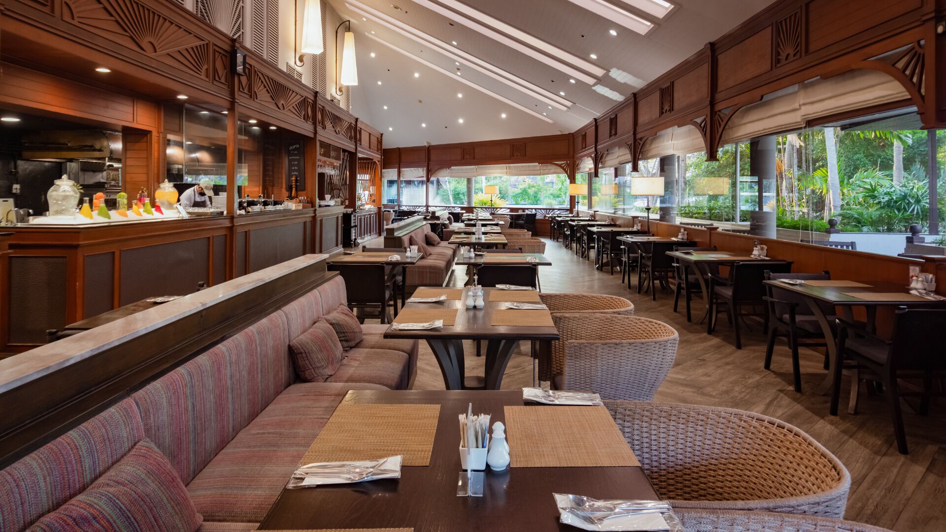A spacious restaurant with high ceilings, wooden paneling, and large windows offering a view of the outdoors.