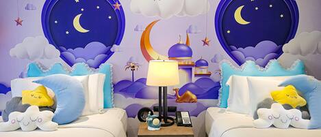 A bedroom with two beds, a nightstand, a lamp, and a wall mural of a night sky with stars and clouds.