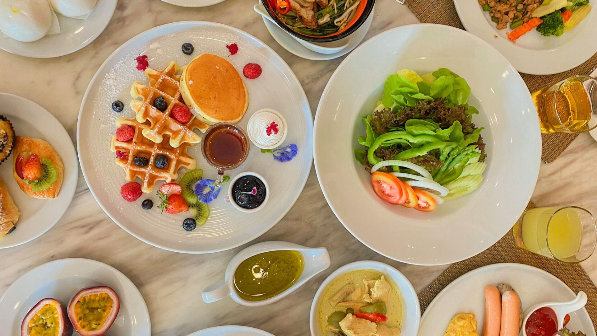 A breakfast buffet with waffles, berries, and various dishes including a salad and soup.