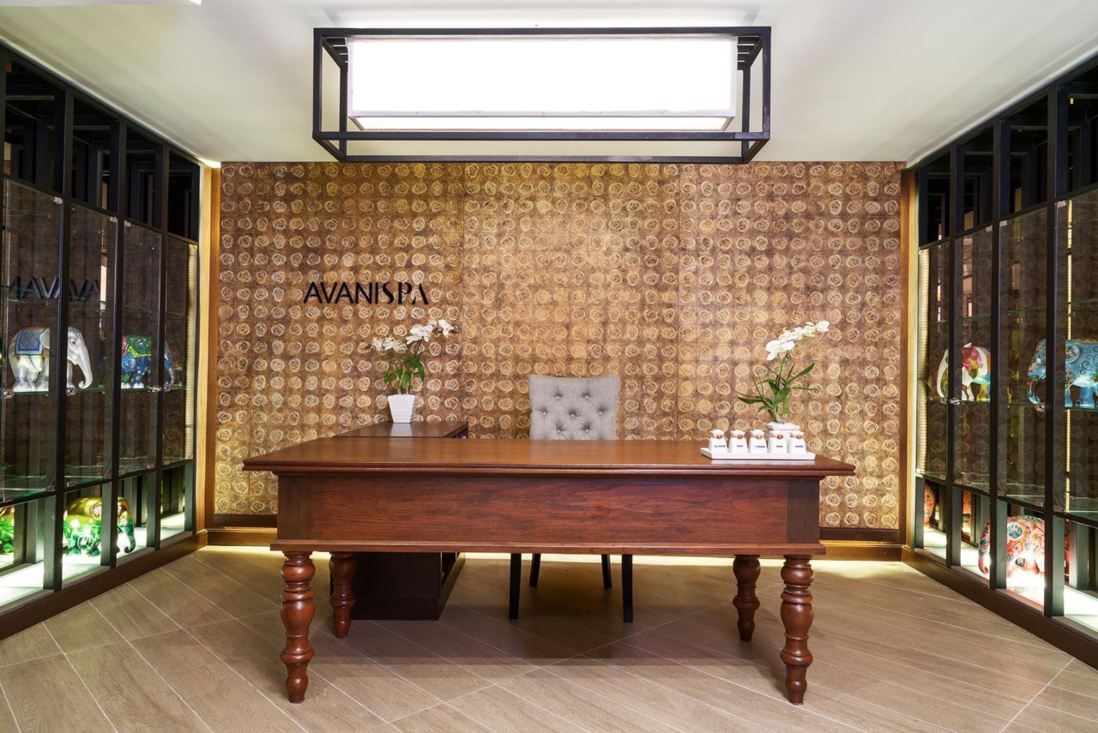 A reception desk with a patterned wallpaper backdrop, a tufted chair, and a potted plant.