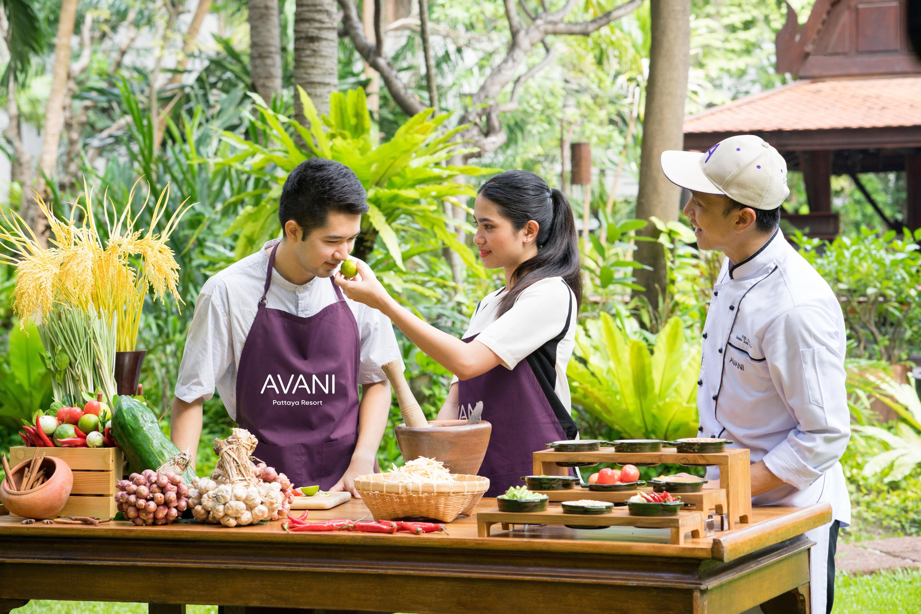 A group of people in aprons around a table with various food items and cooking utensils, indicating a cooking or food preparation activity.
