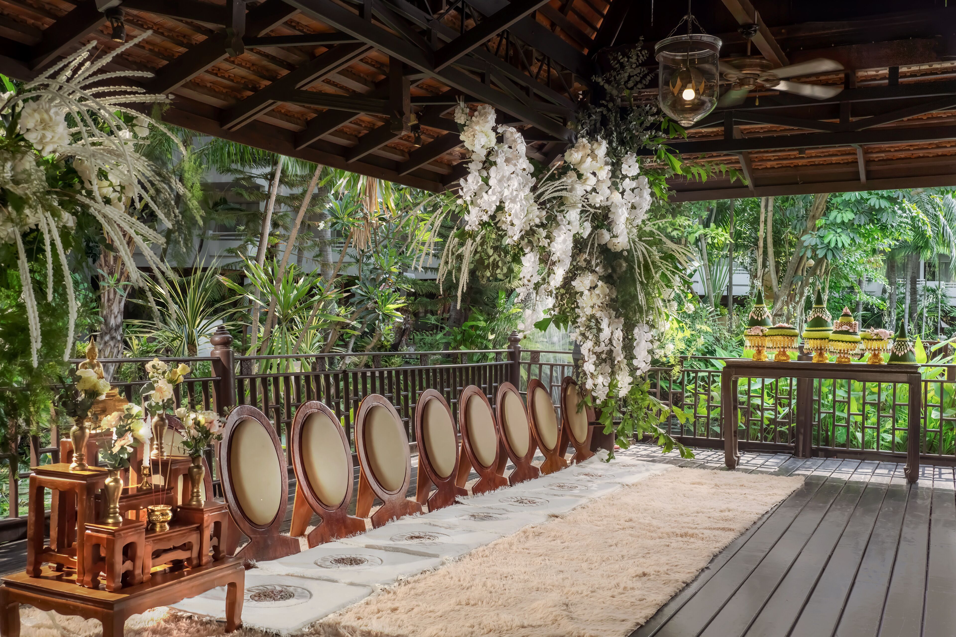 A covered outdoor area with a wooden deck, a row of mirrors, and a decorative table with vases.