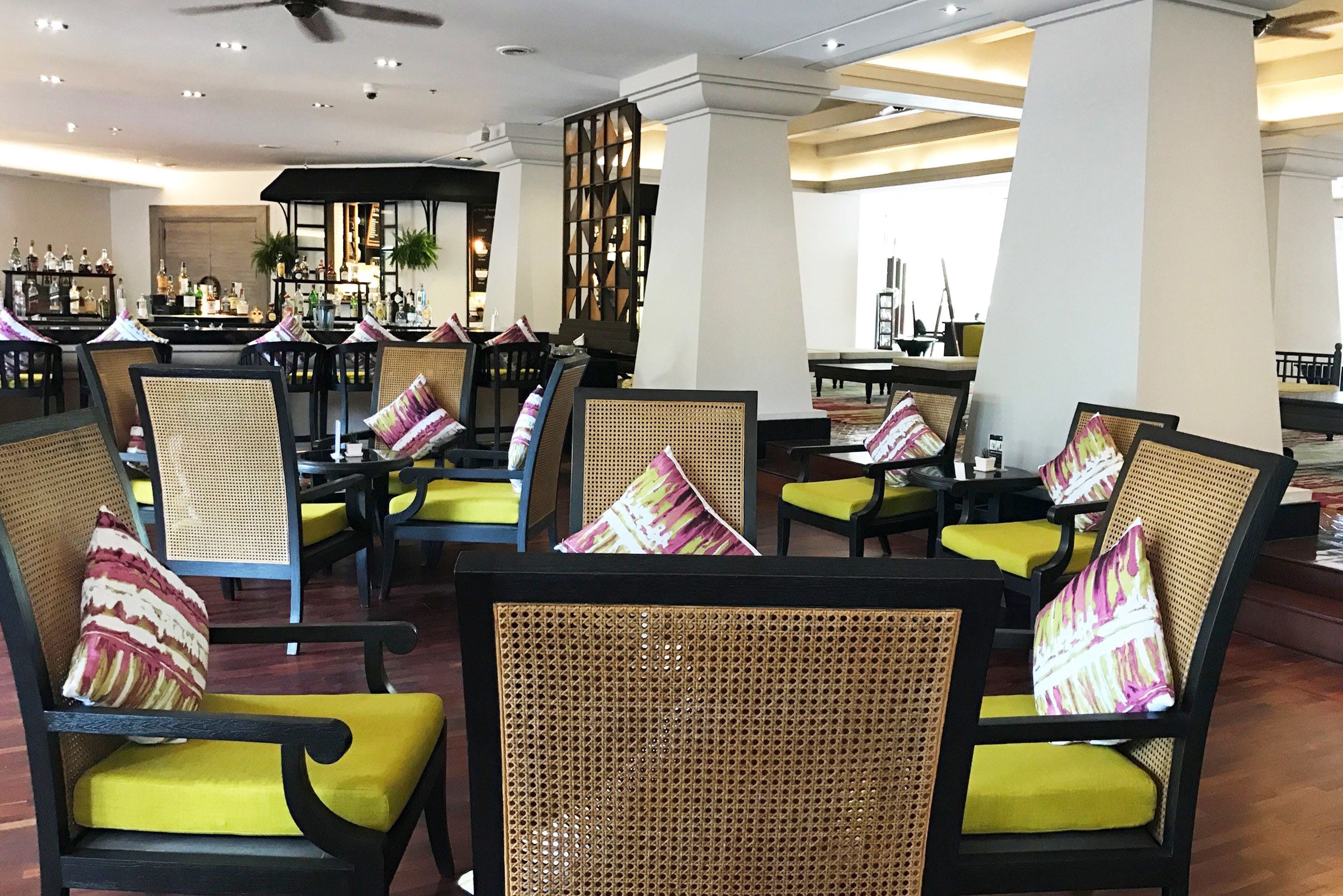 A lobby with wicker chairs and yellow cushions, a bar area with bottles, and a decorative wall.
